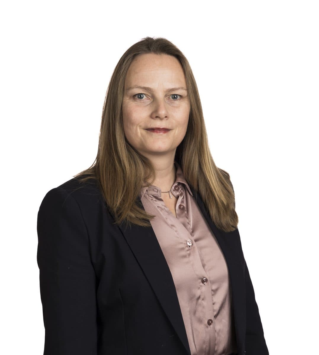 En kvinne med rett, lysebrunt hår, iført mørk blazer over en lys rosa bluse, står mot en enkel, hvit bakgrunn.