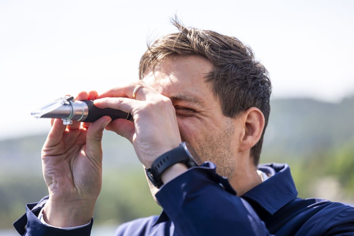 En person holder en håndholdt optisk enhet opp til øyet og ser gjennom den utendørs på en solrik dag.