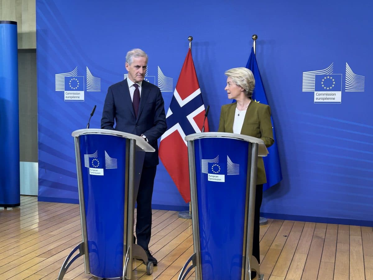 To tjenestemenn står på podier med EU-kommisjonens logoer, med det norske flagget og EU-flagget bak seg, og taler på et pressemøte.