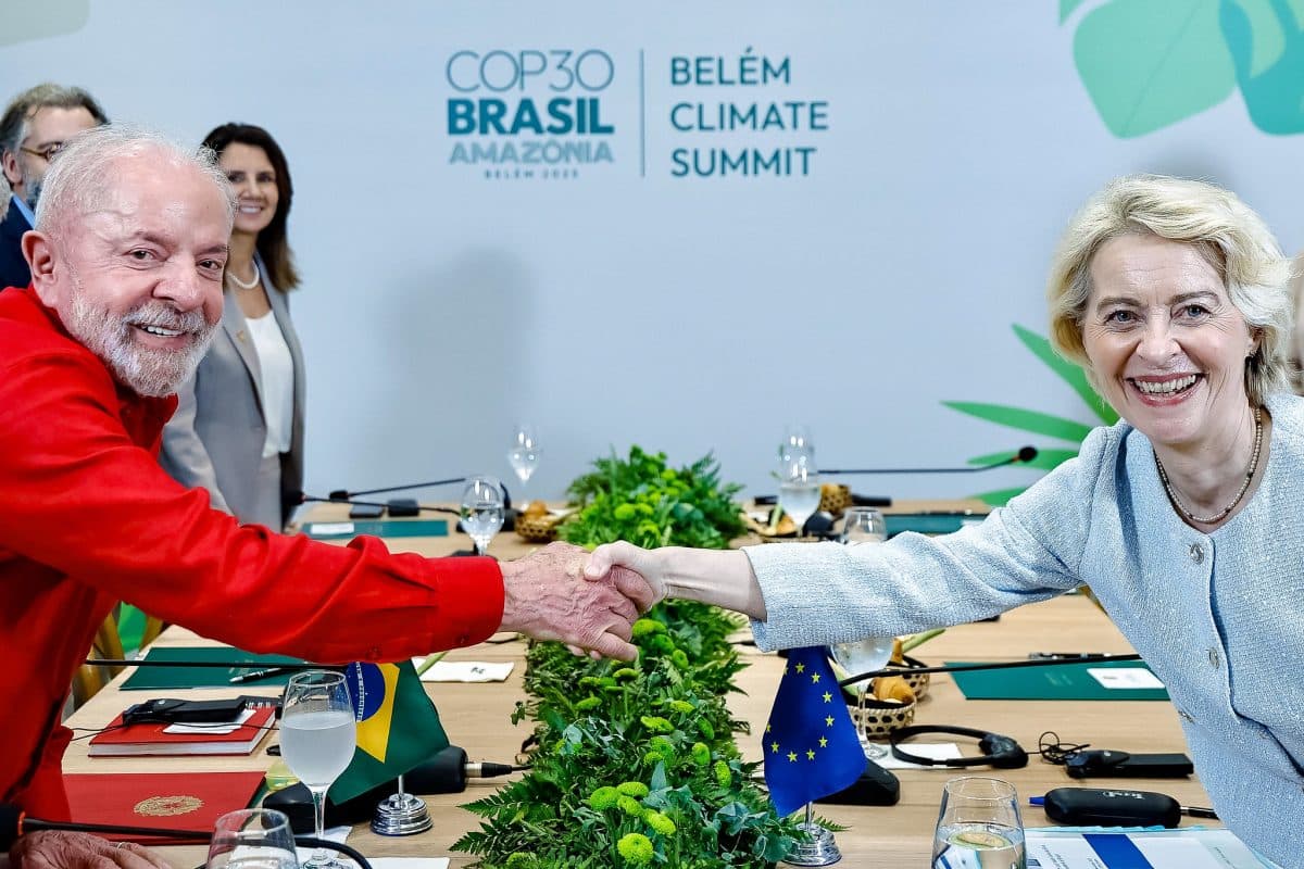 To ledere, en i rødt og en i hvitt, tar hverandre i hånden over et konferansebord på klimatoppmøtet i Belém, mens flaggene til Brasil og EU er synlige.