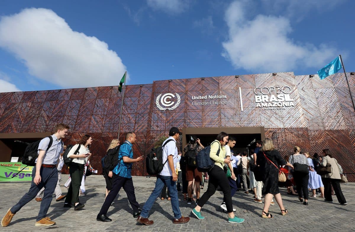 En gruppe mennesker går mot inngangen til en bygning som er merket med FN-skilt for klimaendringer og COP30 Brasil Amazonia under en delvis overskyet himmel.