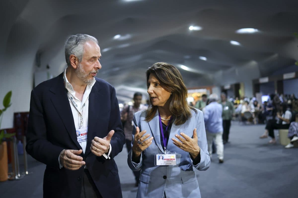 En mann og en kvinne i forretningsklær går og snakker i en travel konferansesal, begge bærer nøkkelbånd med ID-brikker.