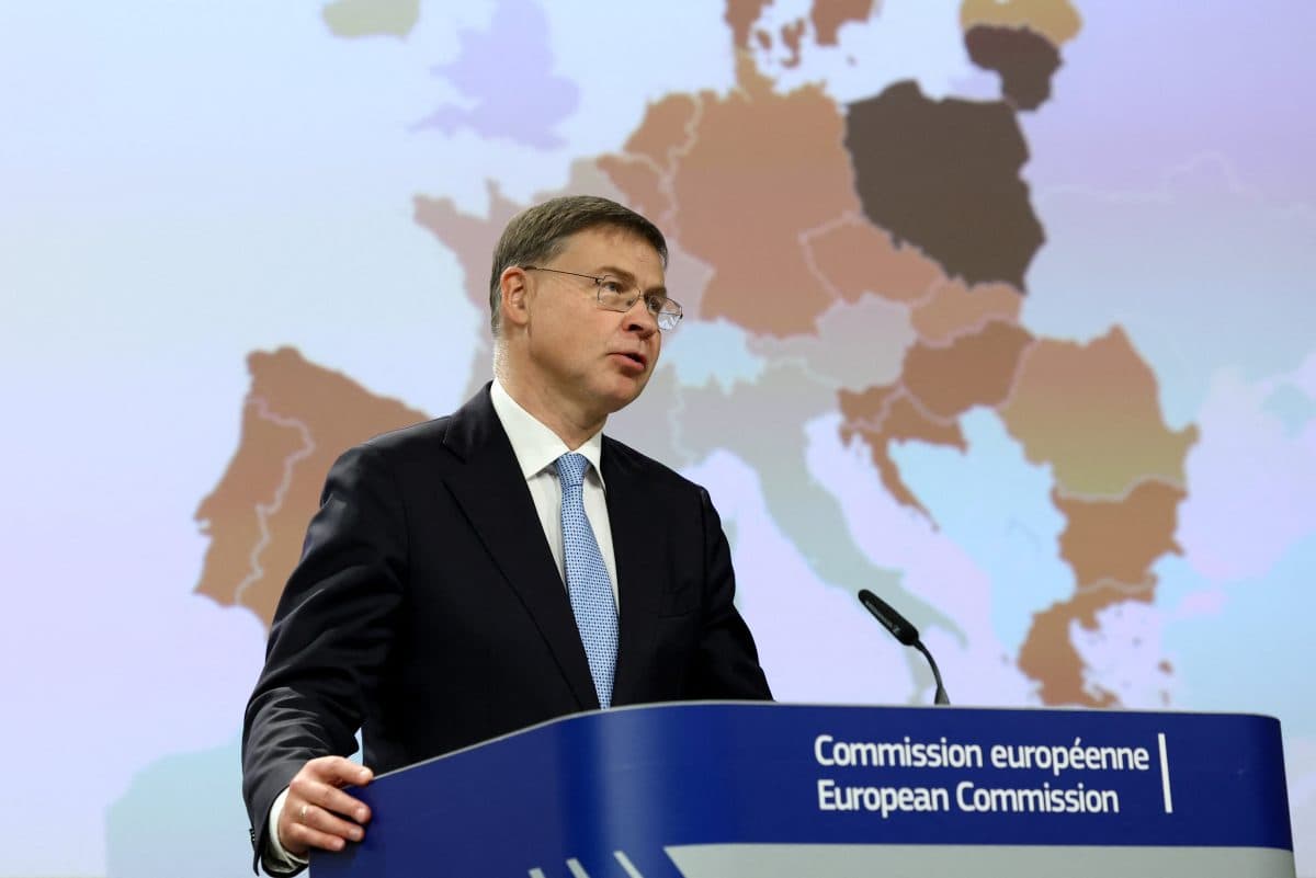 En mann i dress taler på et podium merket "Commission européenne European Commission", med et kart over Europa i bakgrunnen.