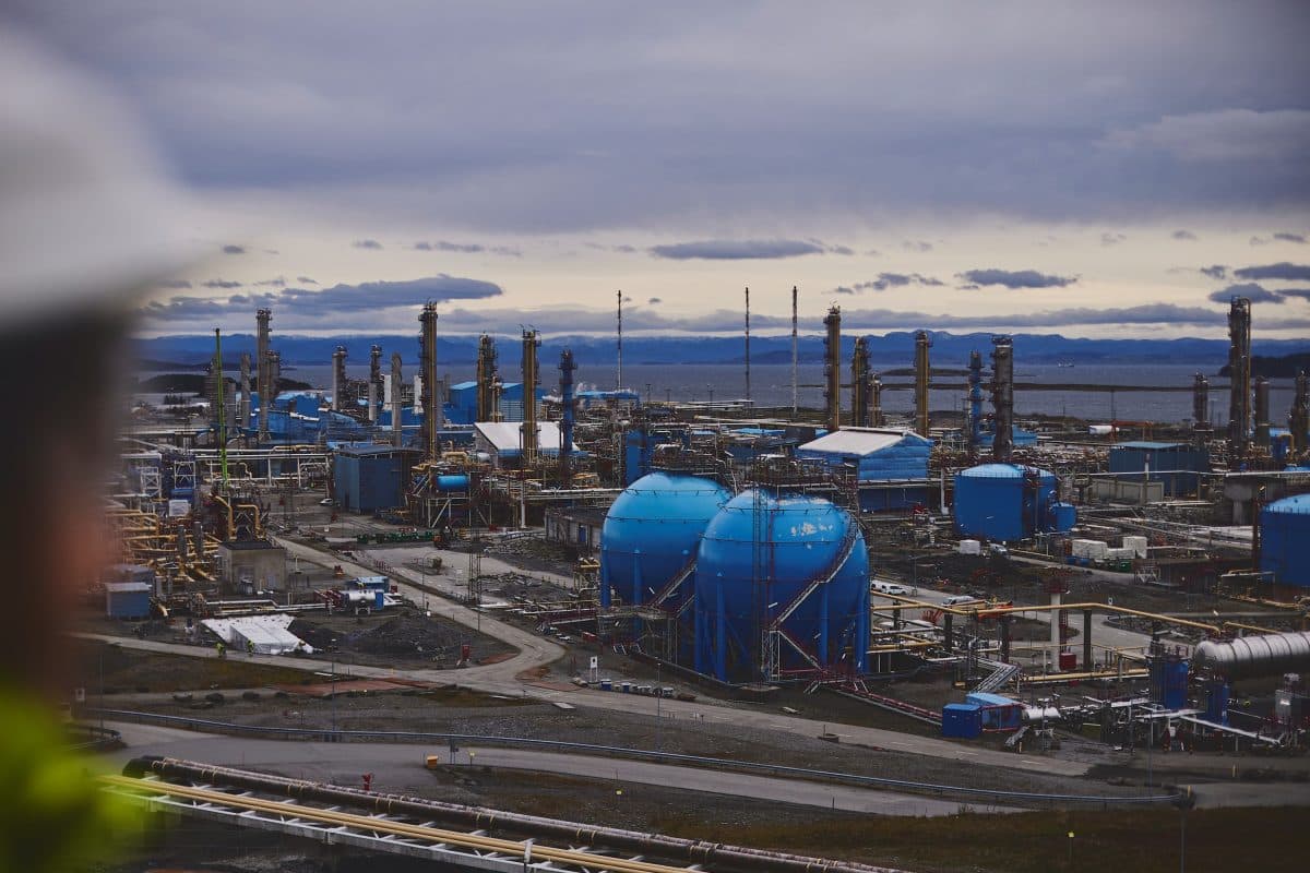 Industrielt raffinerikompleks med flere blå lagertanker, destillasjonstårn og rørledninger under en overskyet himmel.