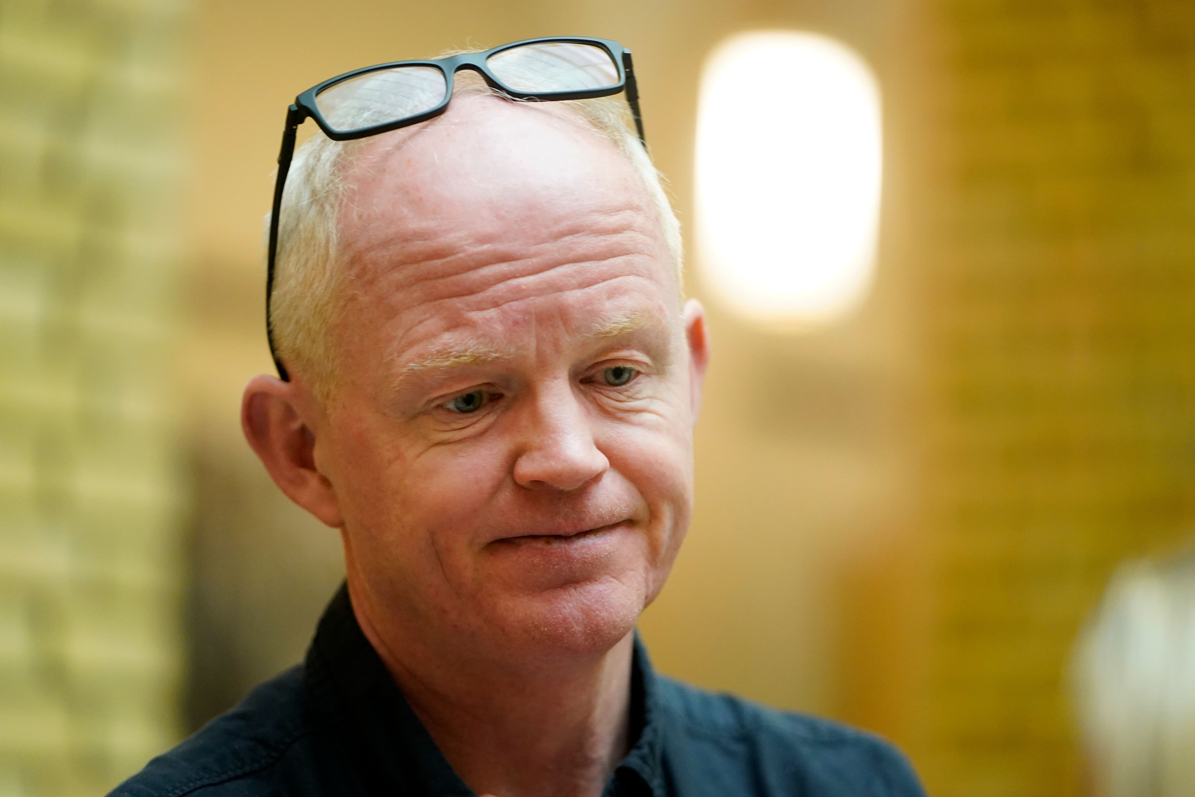 En skallet mann med briller på hodet ser ned med et svakt smil.