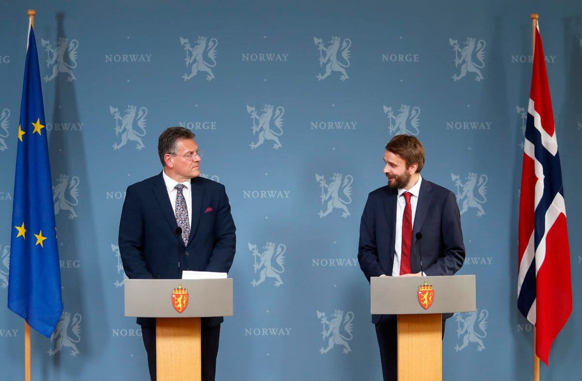 To menn som står ved podier foran flagg.