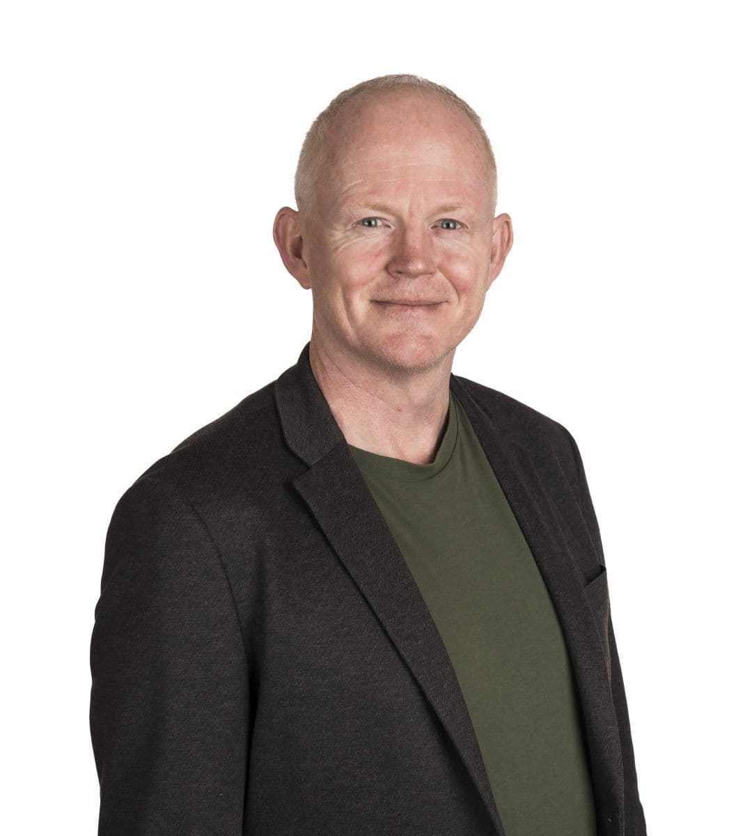 En middelaldrende mann med kort, lyst hår, iført mørk blazer over grønn skjorte, står mot en enkel, hvit bakgrunn og smiler til kameraet.