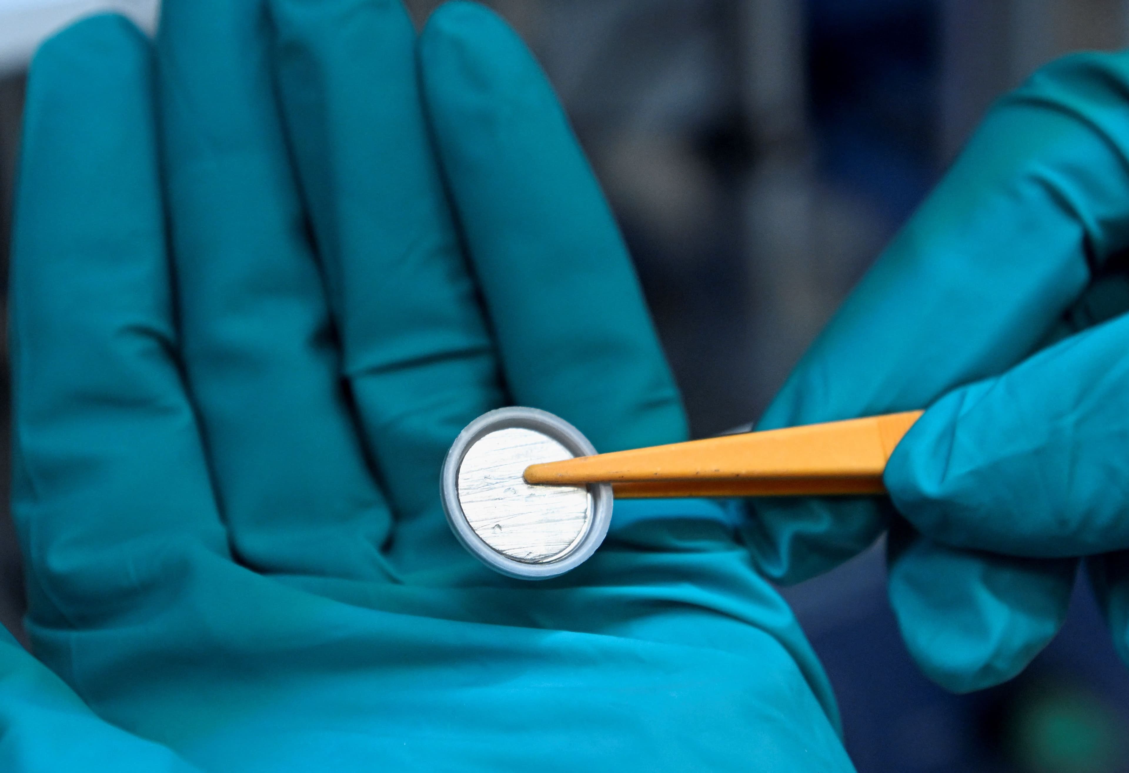 Hender med hansker holder en battericelle i nærbilde.