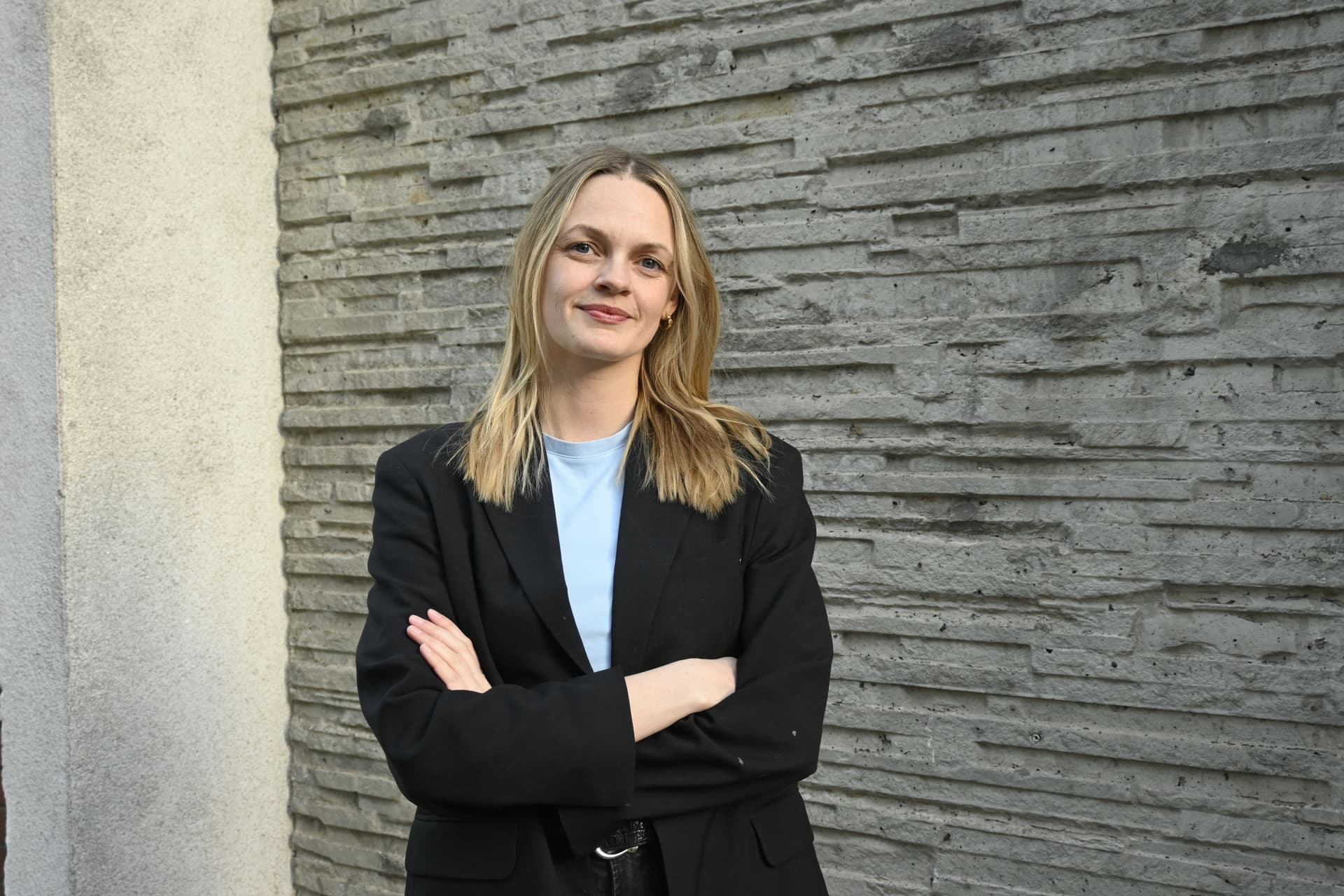 En kvinne som står med kryssede armer foran en grå vegg